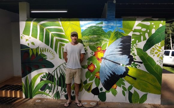TRACQS participant Darren standing in front of a colourful butterfly mural he painted