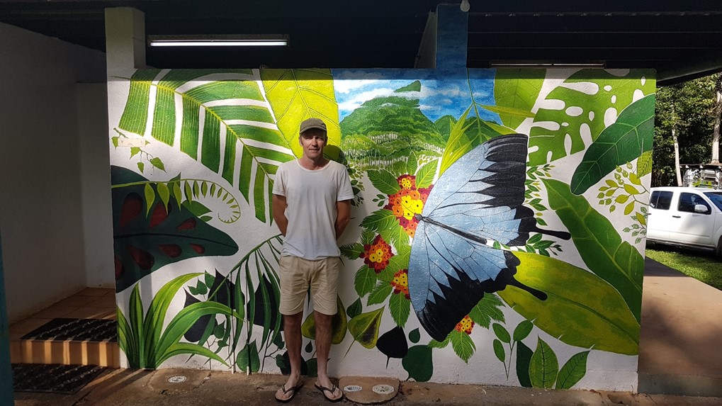 TRACQS participant Darren standing in front of the colourful butterfly mural he painted